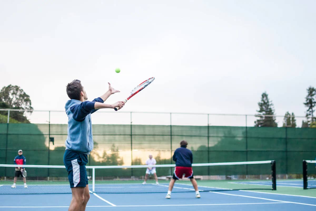 Four players in a doubles match on a sunlit court